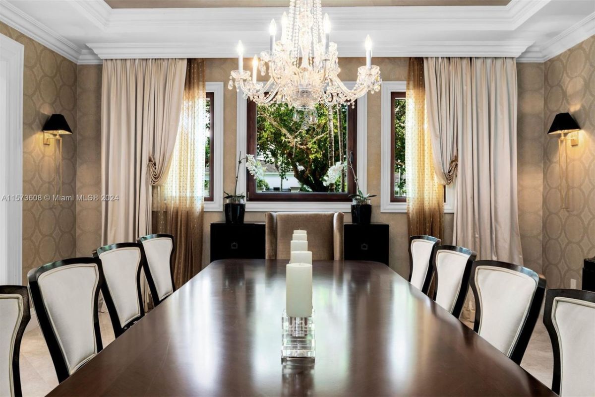 A dining room with a window, chandelier, and a dining table surrounded by chairs.