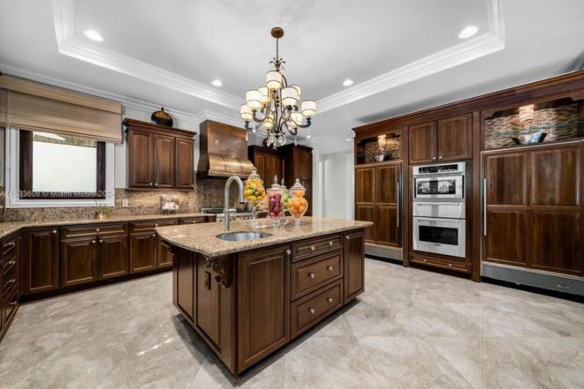 A kitchen with an island, countertops, a chandelier, cabinets, and kitchen appliances.