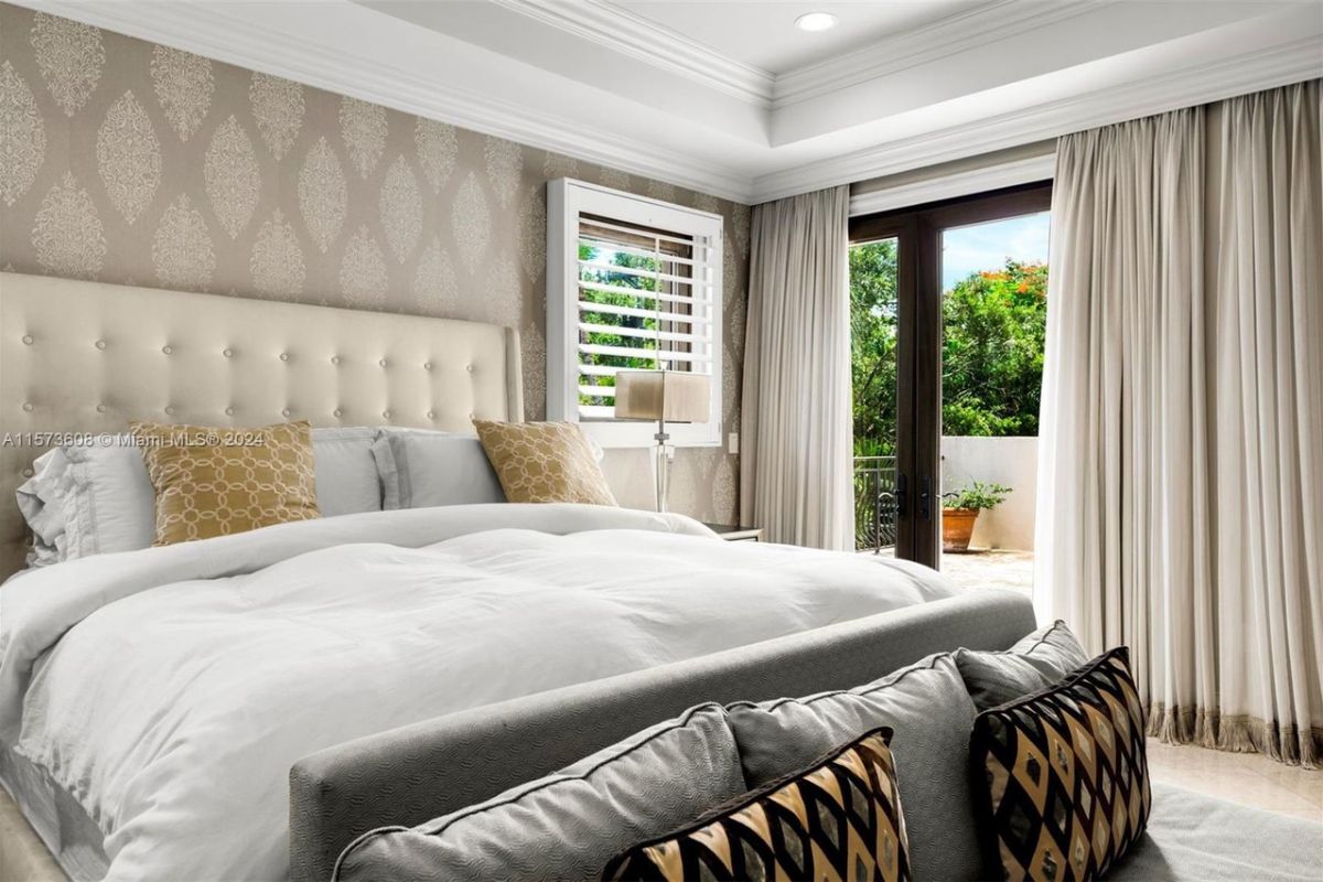 A bedroom with a bed with a headboard, wallpaper, a window, and lampshades.