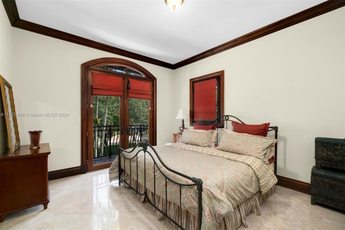 A bedroom with a bed, tiled floor, cabinet, and mirror.