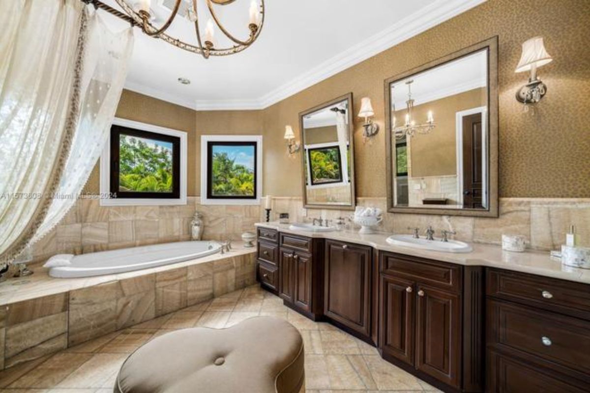 A bathroom with dual vanity, mirror, cabinets, windows, and bathtub.