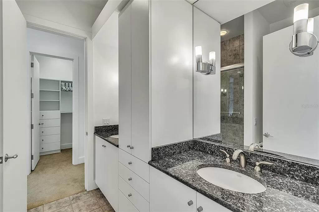 Bathroom with a walk-in closet and a dual sink vanity with a linen closet in the middle.