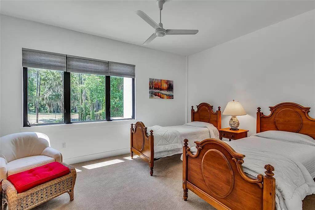 Bedroom with two wooden beds and a round back chair with a tufted stool.