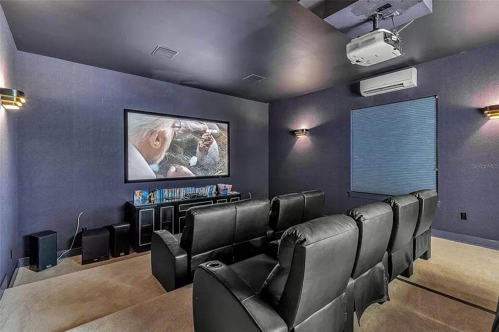 Home theater with black leather recliners over the carpeted floor.