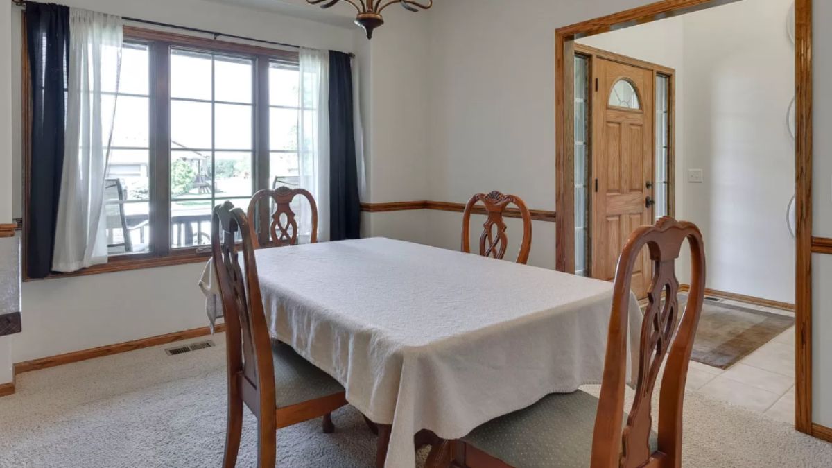 A dining room with windows and a dining table surrounded by chairs.