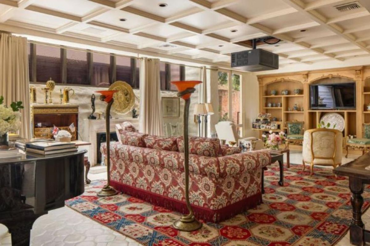 A living room with a ceiling with molding, a rug, a piano, a fireplace, a TV, shelves, cabinets, a couch, chairs, and a center table.