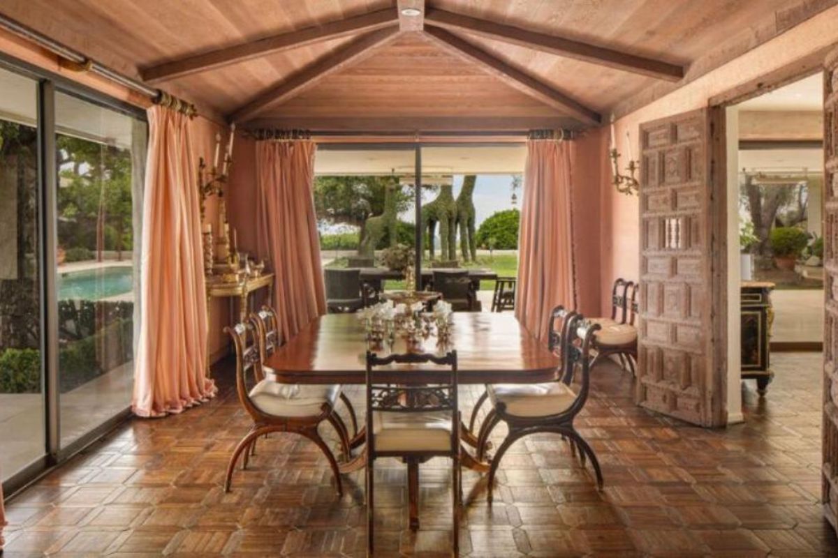 A dining room with an exposed beam ceiling, glass sliding doors, and a dining table surrounded by chairs.