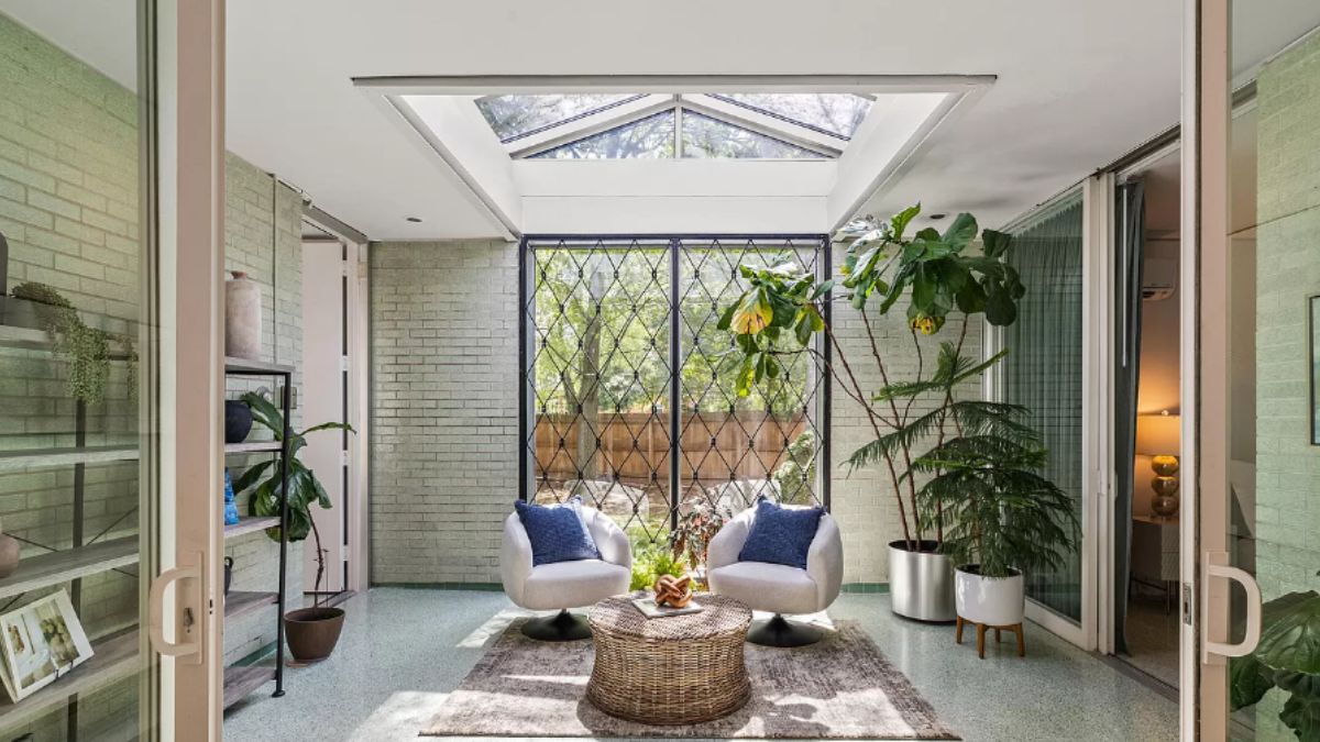 An atrium with houseplants, skylight roofing, and chairs.