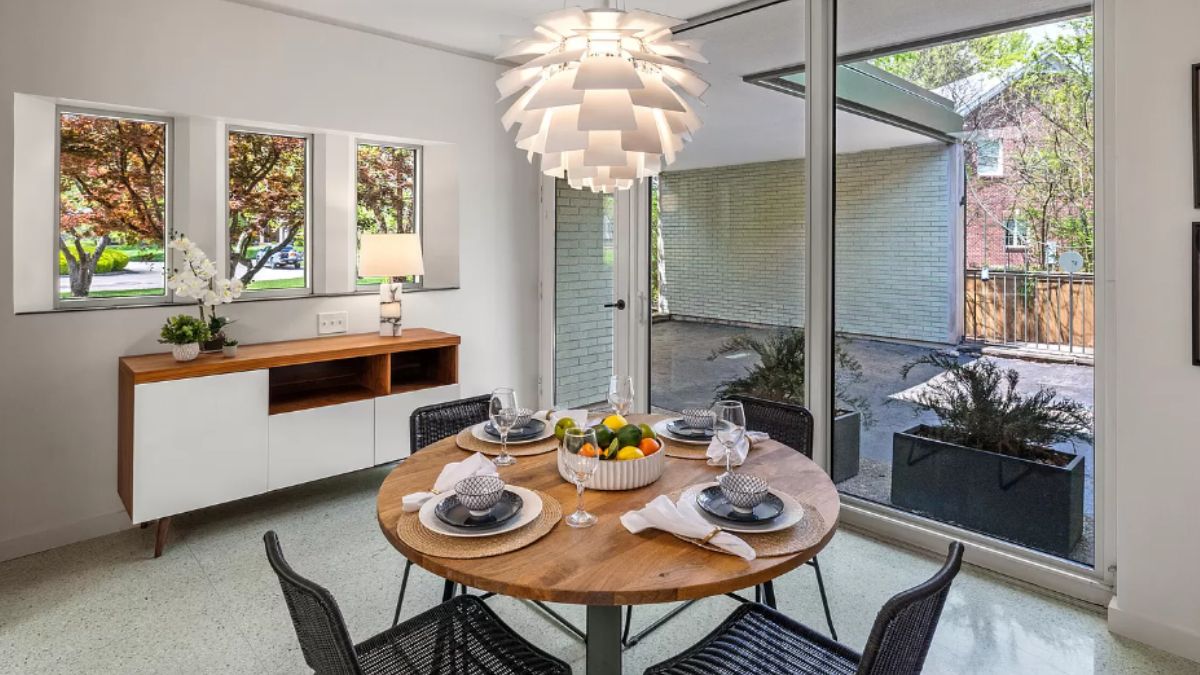 A dining room with cabinets, windows, a chandelier, and a round table surrounded by chairs.