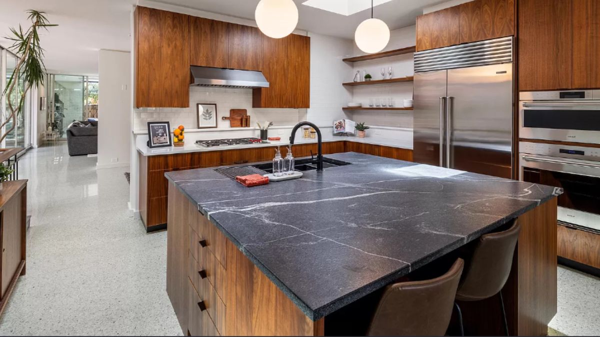 A kitchen with a center island, chairs, sink, cabinets, and kitchen appliances.