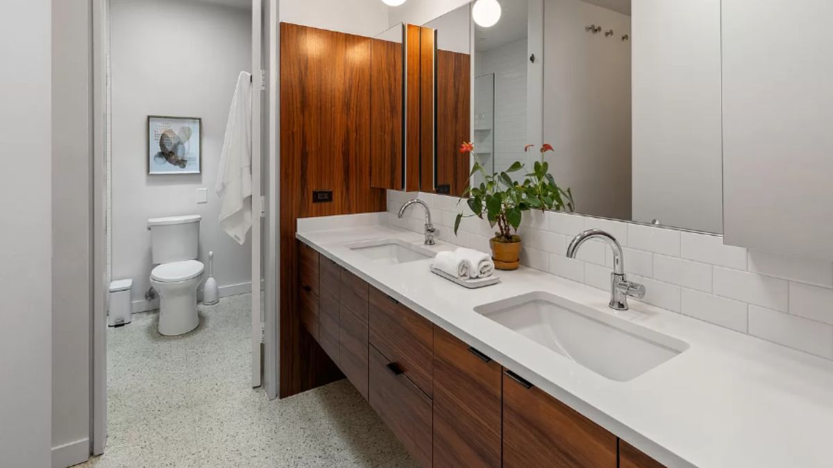 A bathroom with a vanity, mirror, cabinet, and toilet.