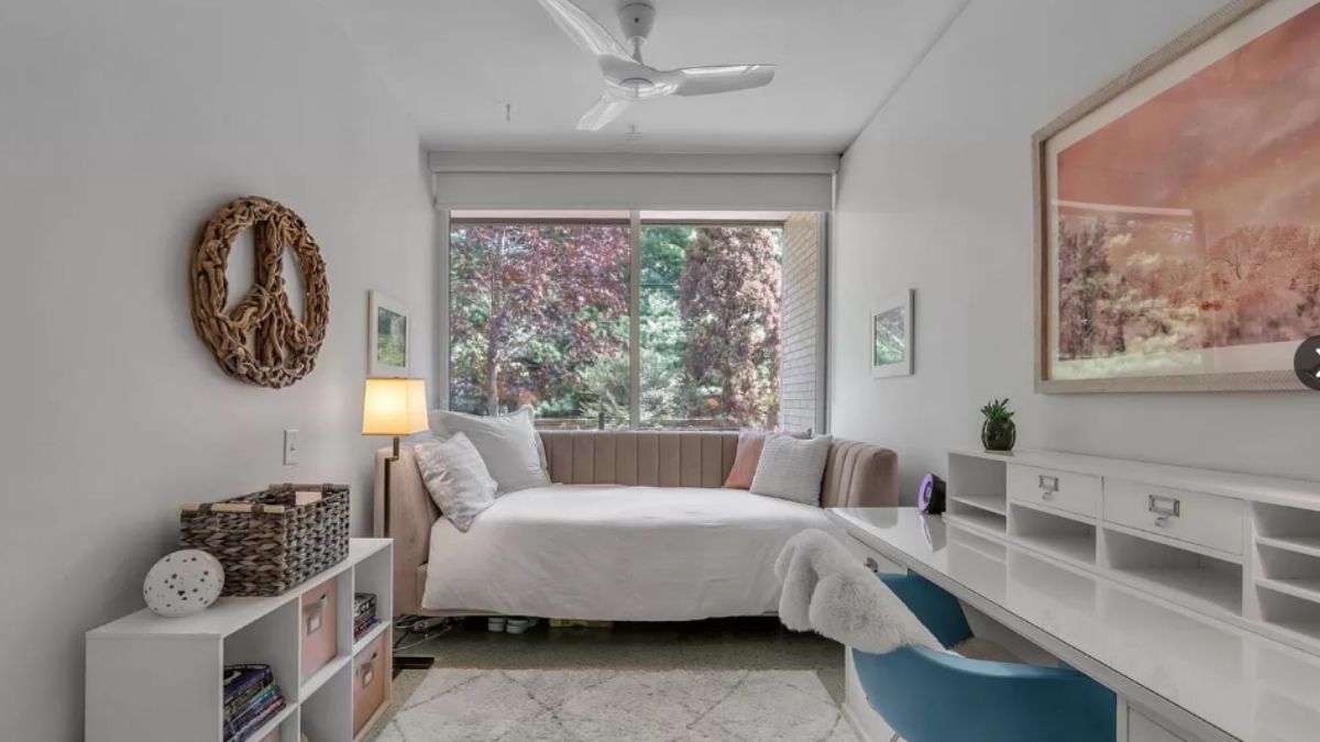 A bedroom with a painting, cabinets, windows, and a ceiling fan.