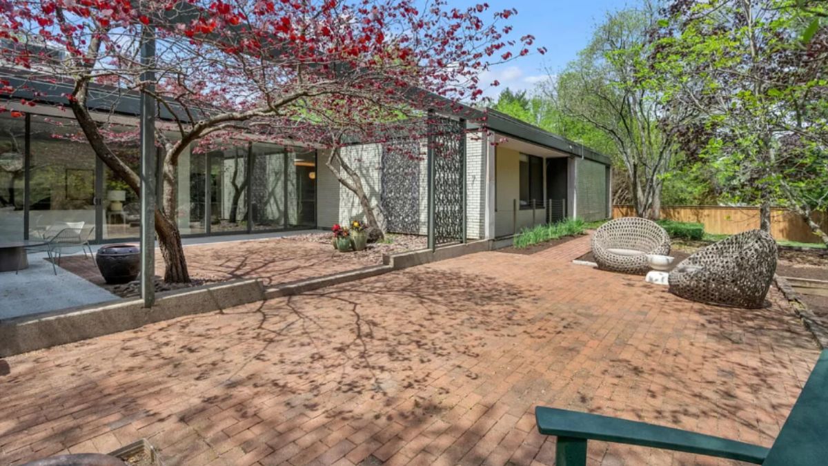 A patio with a brick floor, chair, and a tree.