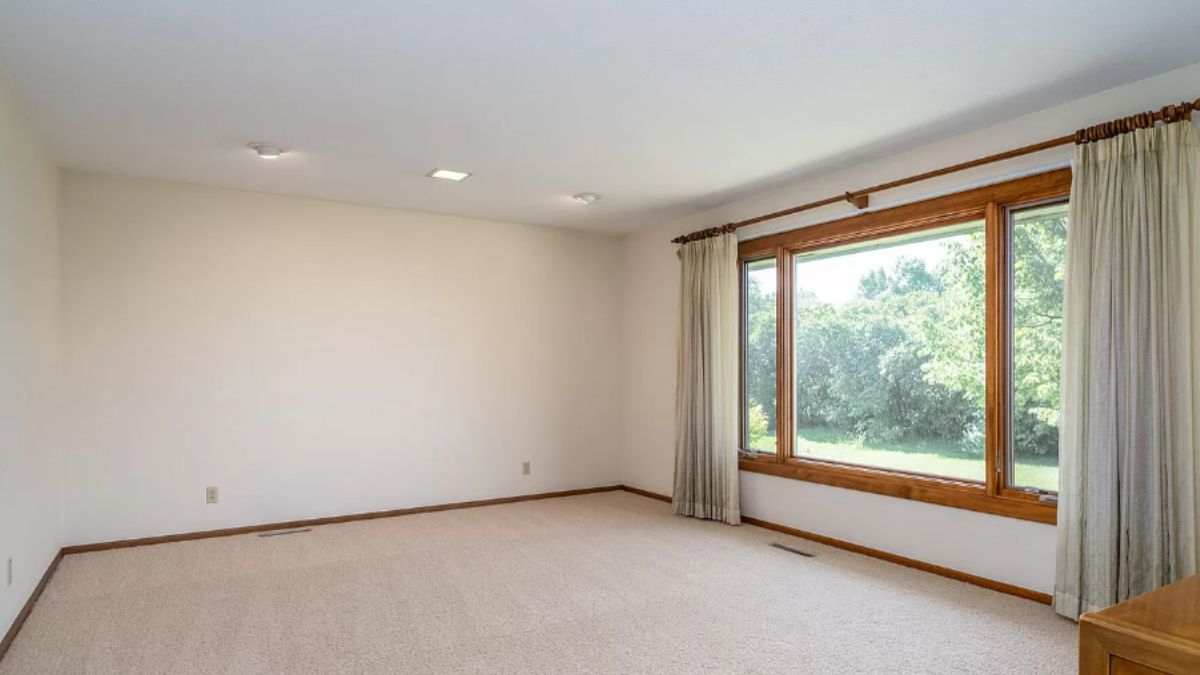 A living room with a window, white walls, and a white ceiling.