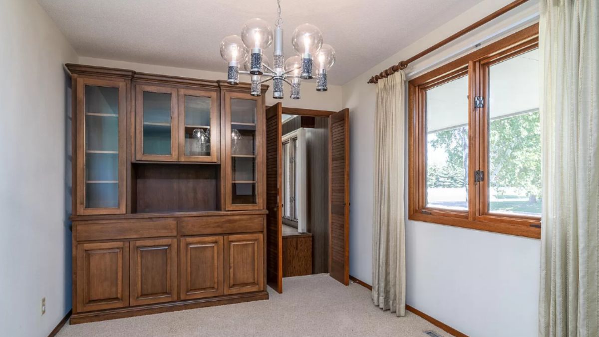 A dining room with a cabinet, window, and chandelier.