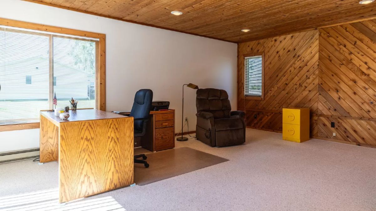 A home office with a window, wooden ceiling, studio couch, drawers, desk, and chair.