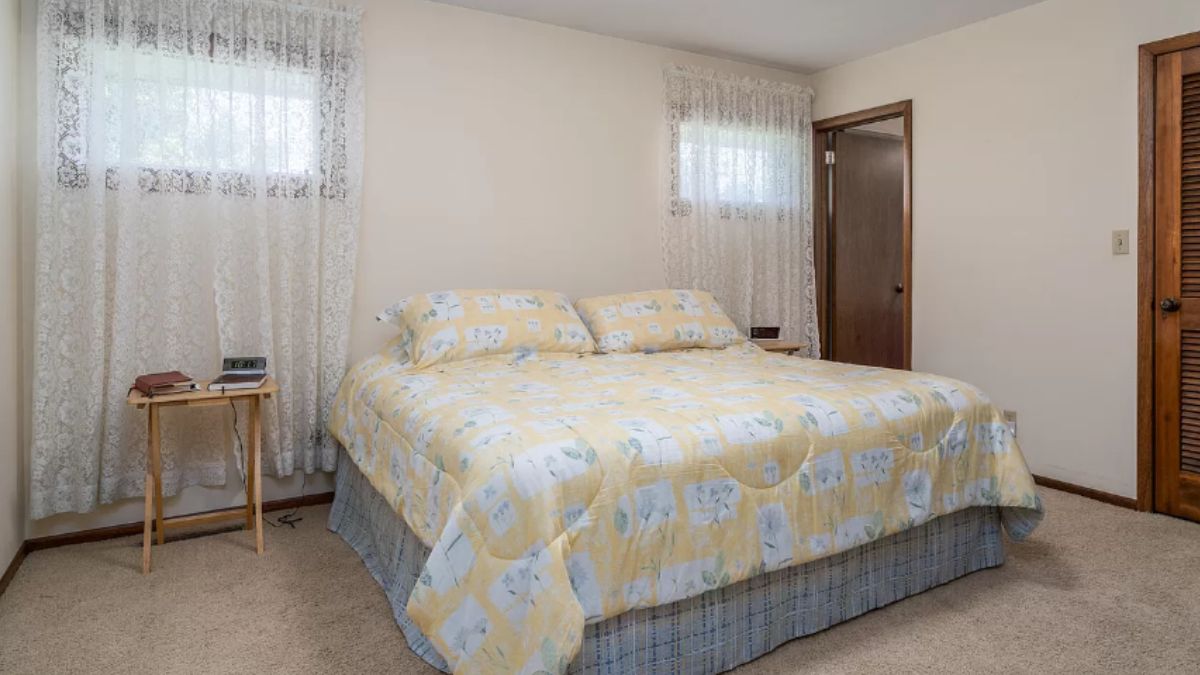 A bedroom with a bed, windows, and a side table.