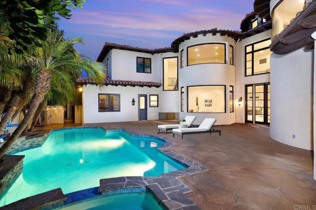 A swimming pool with a jacuzzi, chairs, and trees on the poolside.