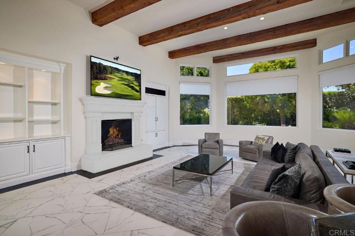 A living room with an exposed beam ceiling, fireplace, TV, shelf, and cabinets.