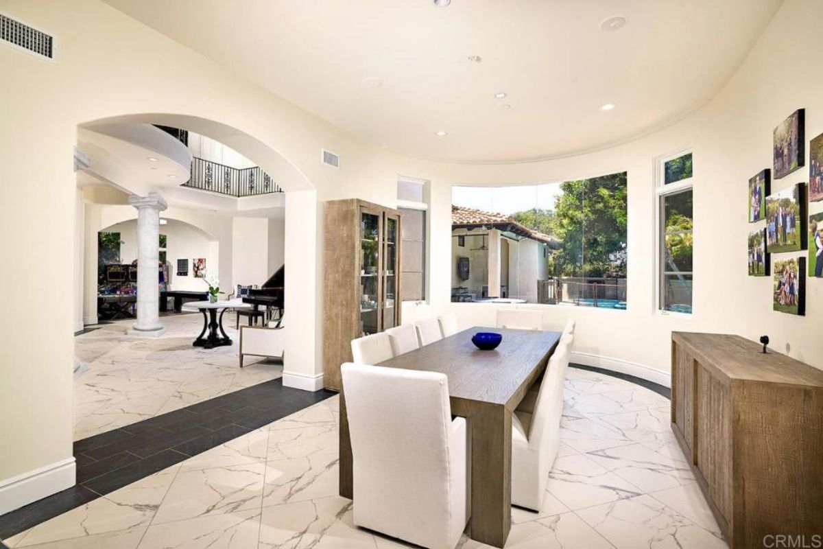 A dining room with tiled floor, cabinets, windows, and a dining table surrounded by chairs.