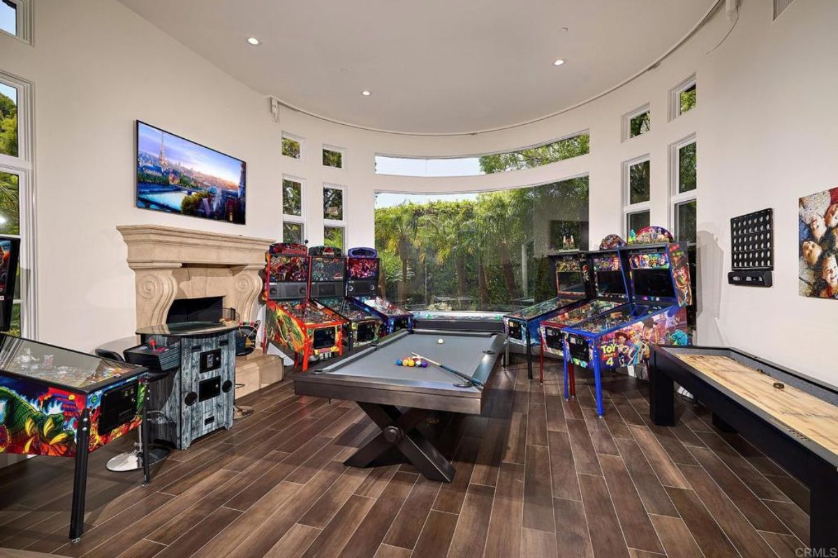 A game room with a TV, fireplace, arcade games, and a pool table.