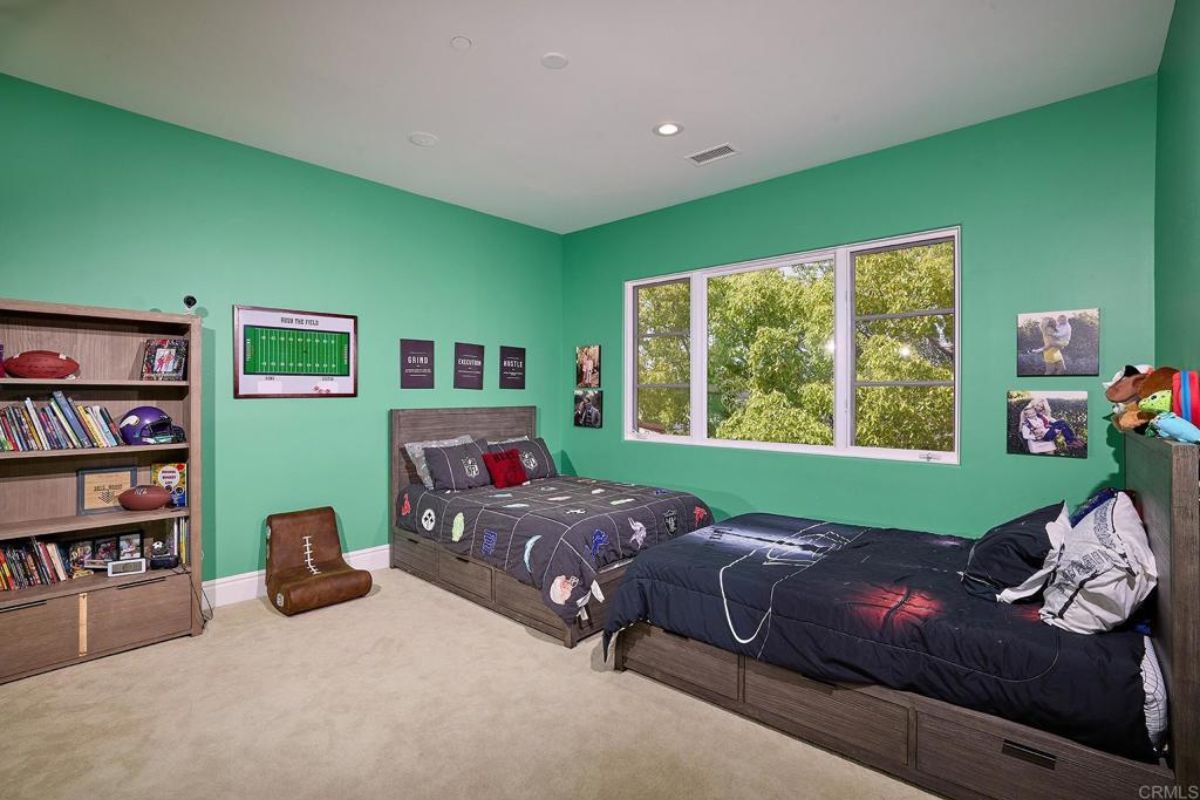 A bedroom with two beds, a shelf, a window, and green walls.