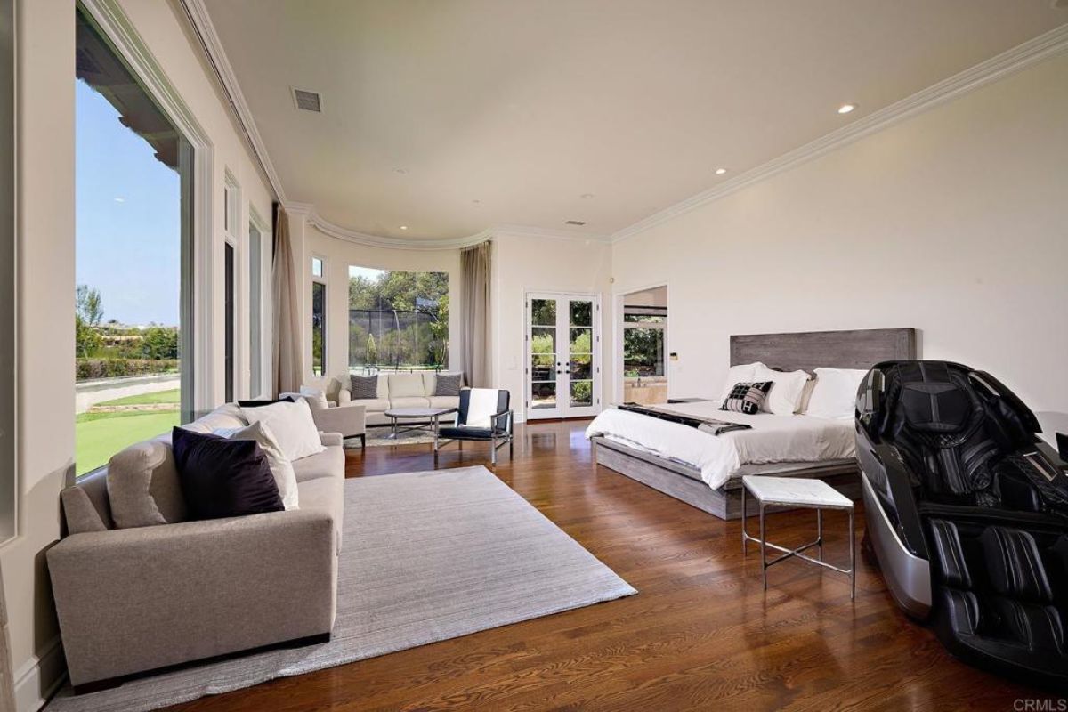 A bedroom with a bed, couches, chairs, windows, a coffee table, and a massage chair.