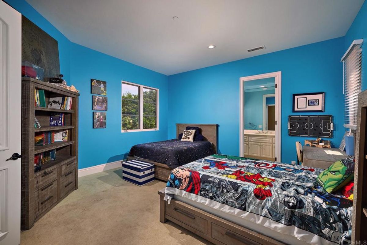 A bedroom with two beds, windows, a shelf, a desk, and a chair.