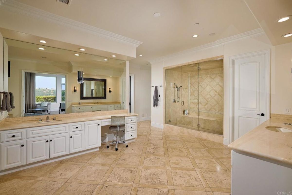 A bathroom with a tiled floor, vanity, countertop, cabinets, chair, and mirror.