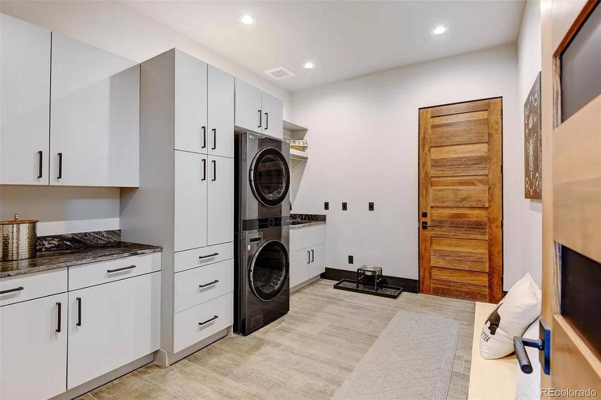 Laundry room with white cabinets, marble counters, and a stacked washer and dryer.