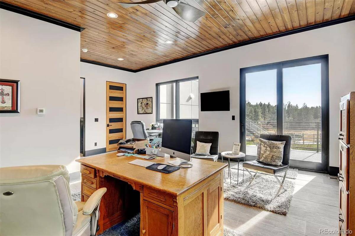 Home office with a wooden desk, leather chairs, and sliding glass doors that open to the rear patio.