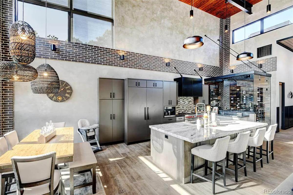 Kitchen and dining area under a tall ceiling adorned with industrial pendants.