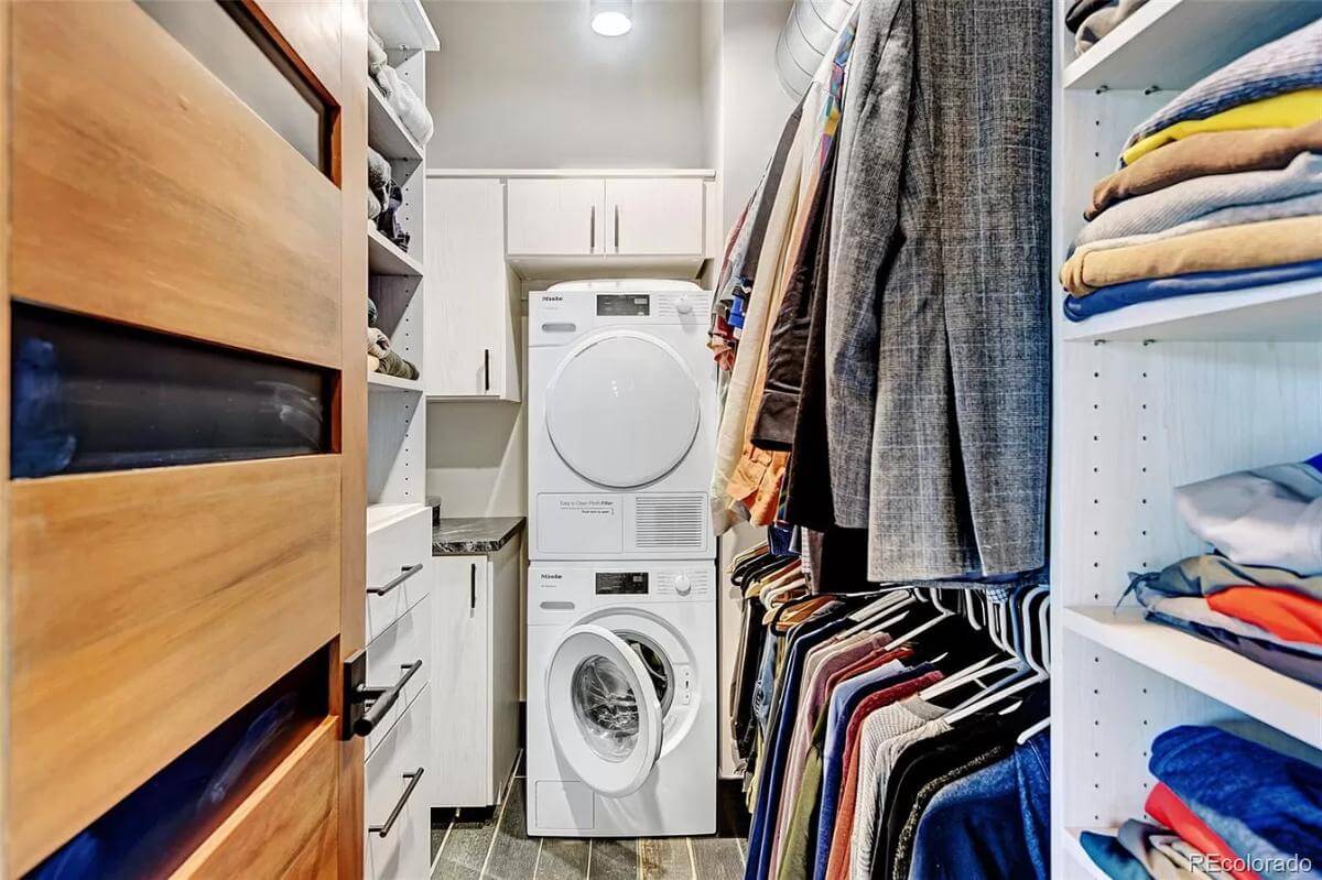 His walk-in closet with white cabinets and a stacked washer and dryer.