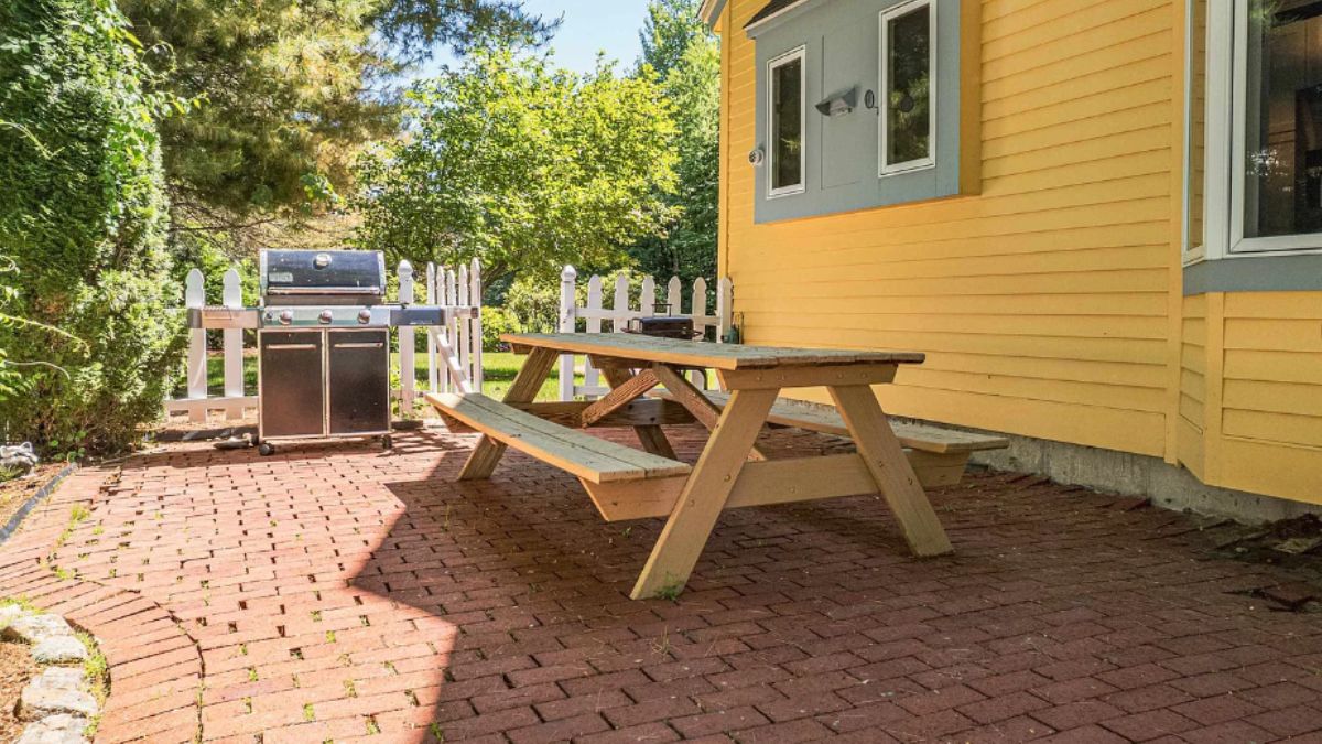 A patio with a table with a bench, brick floor, and a griller