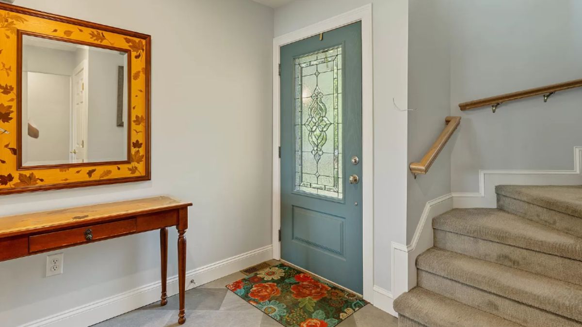 A foyer with a mirror, rug, and staircase.