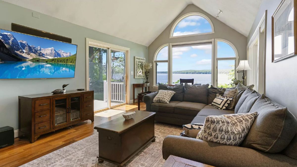 A living room with a vaulted ceiling, windows, TV, cabinet, rug, couch, and center table.