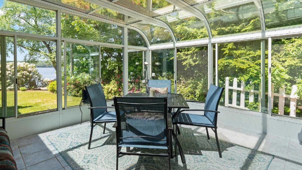 A sunroom with glass walls, a glass ceiling, and a table surrounded by chairs.