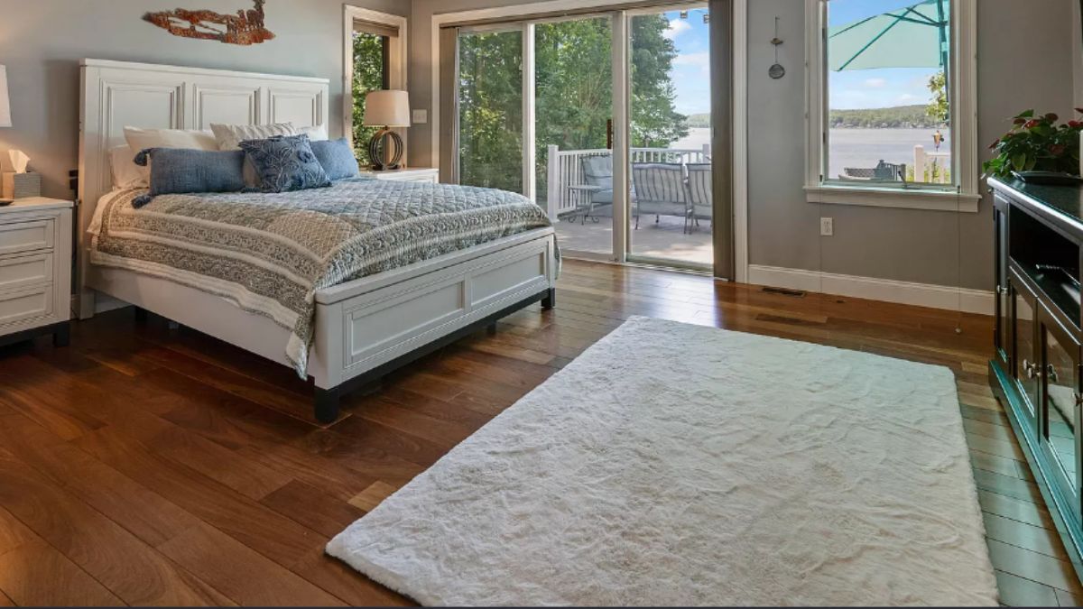 A bedroom with a bed, nightstand, wooden floor, and rug.