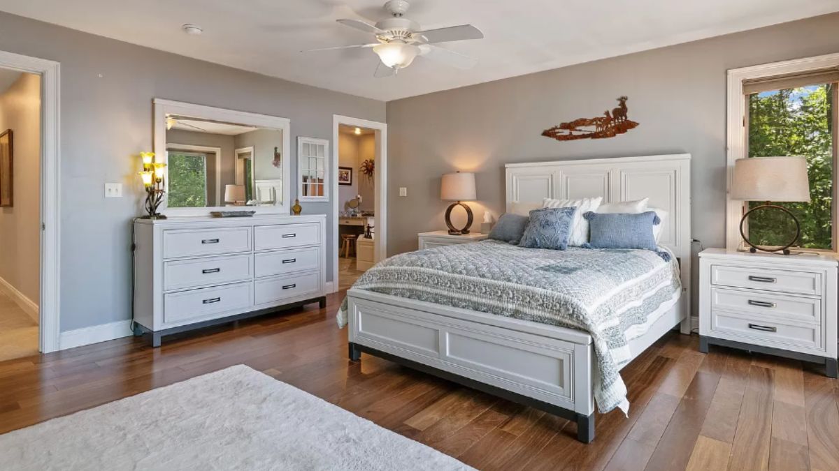 A bedroom with a bed, ceiling fan, nightstand, cabinets, and lampshades.