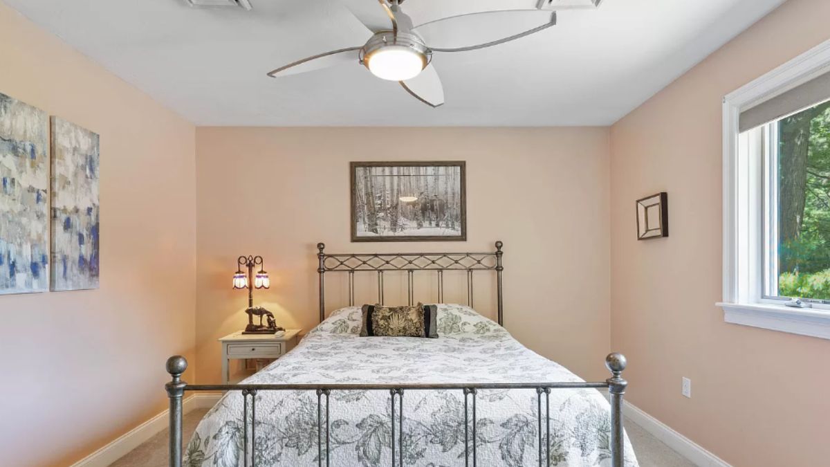 A bedroom with a bed, ceiling fan, nightstand, and paintings.