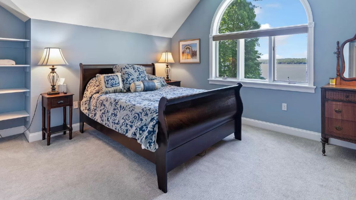 A bedroom with a bed, windows, shelf, nightstand, and cabinet.