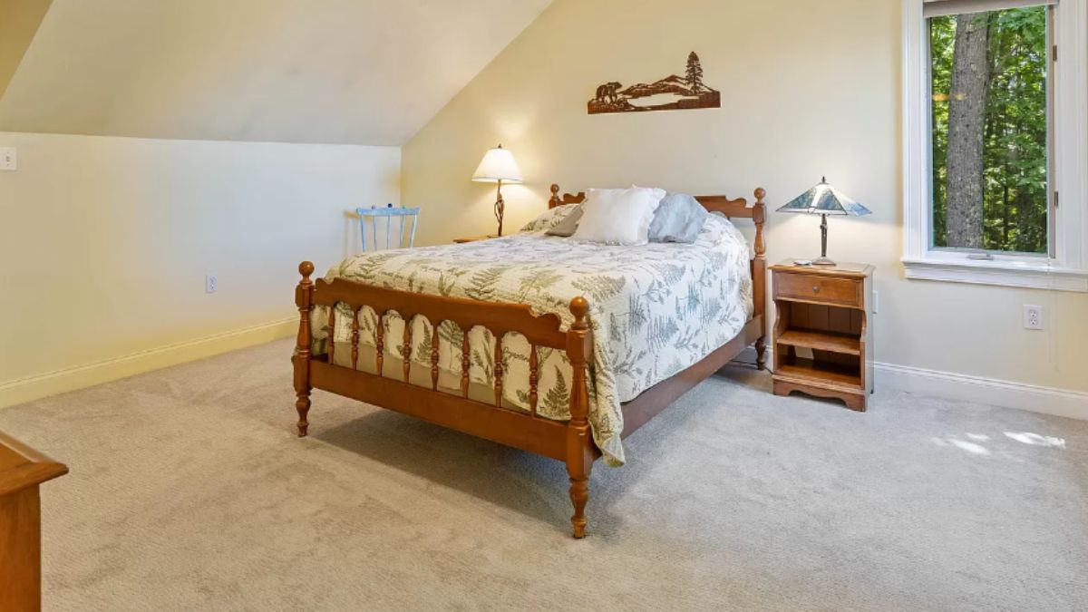 A bedroom with a bed, window, nightstand, and lampshades.