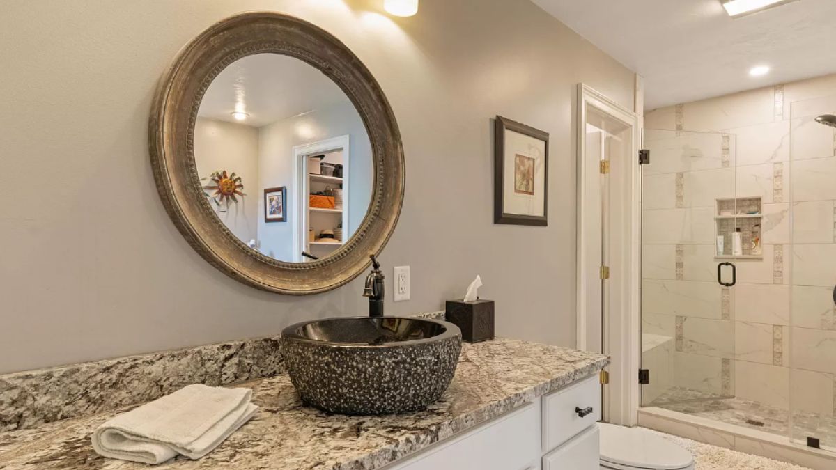 A bathroom with a vanity, mirror, toilet, and shower room.