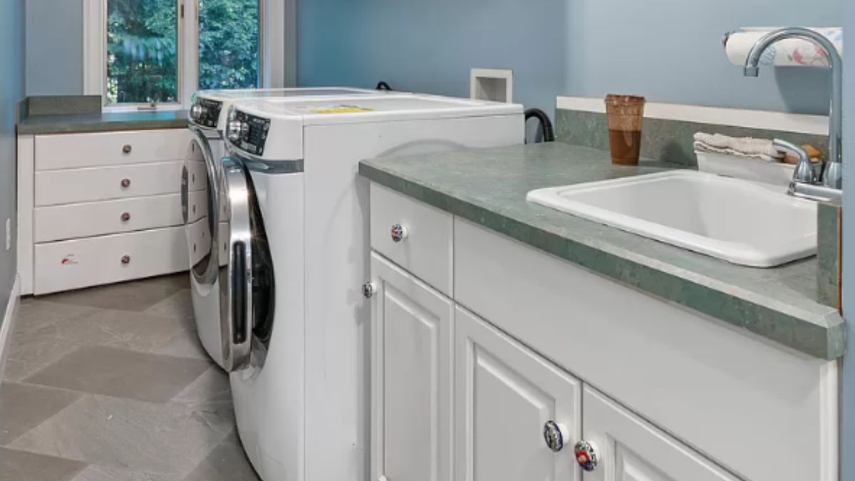 A laundry room with a countertop, sink, cabinets, and washing machine.