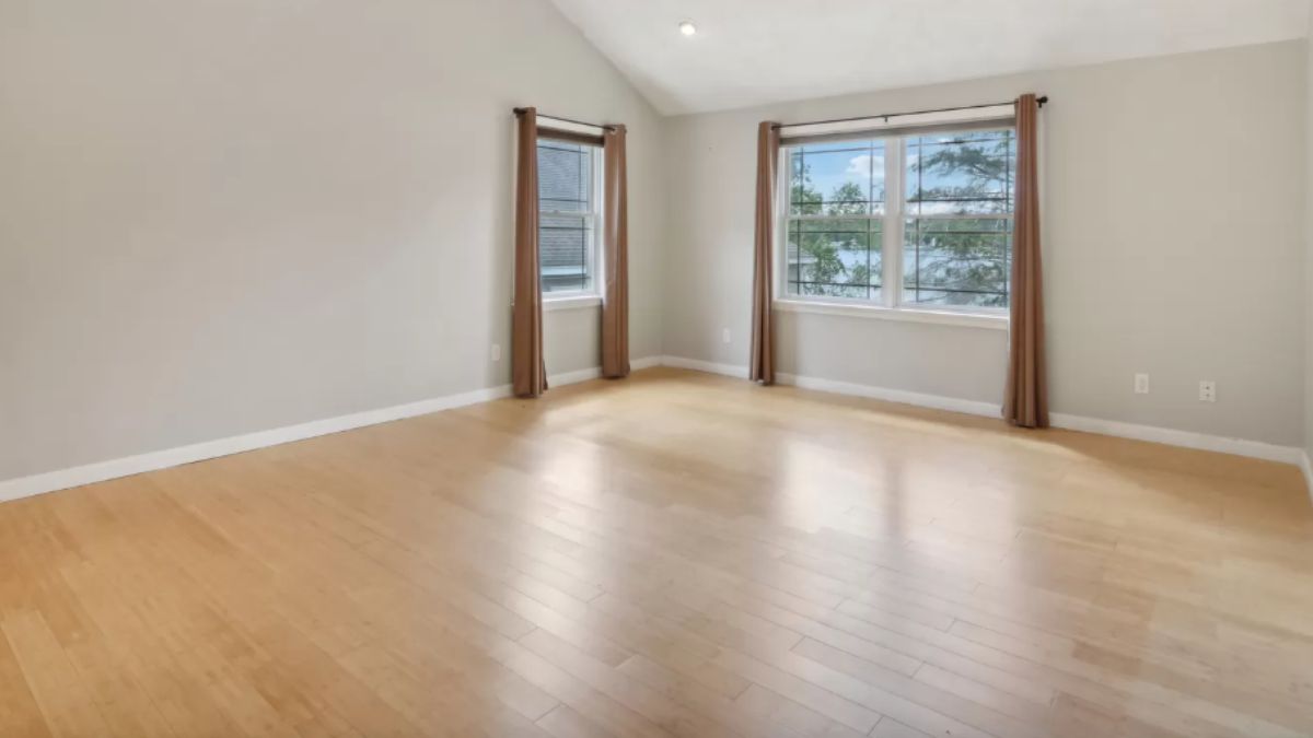 An empty bedroom with a wooden floor and windows.