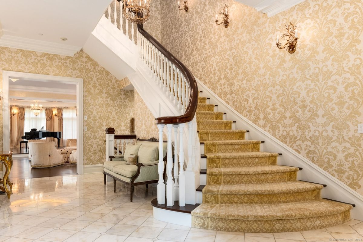 A foyer with wallpaper, a tiled floor, a couch, and a staircase.