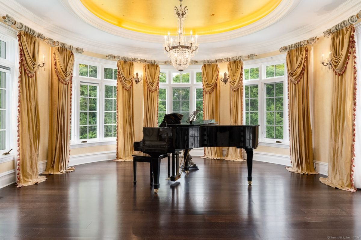 A piano room with a piano, chandelier, and windows.