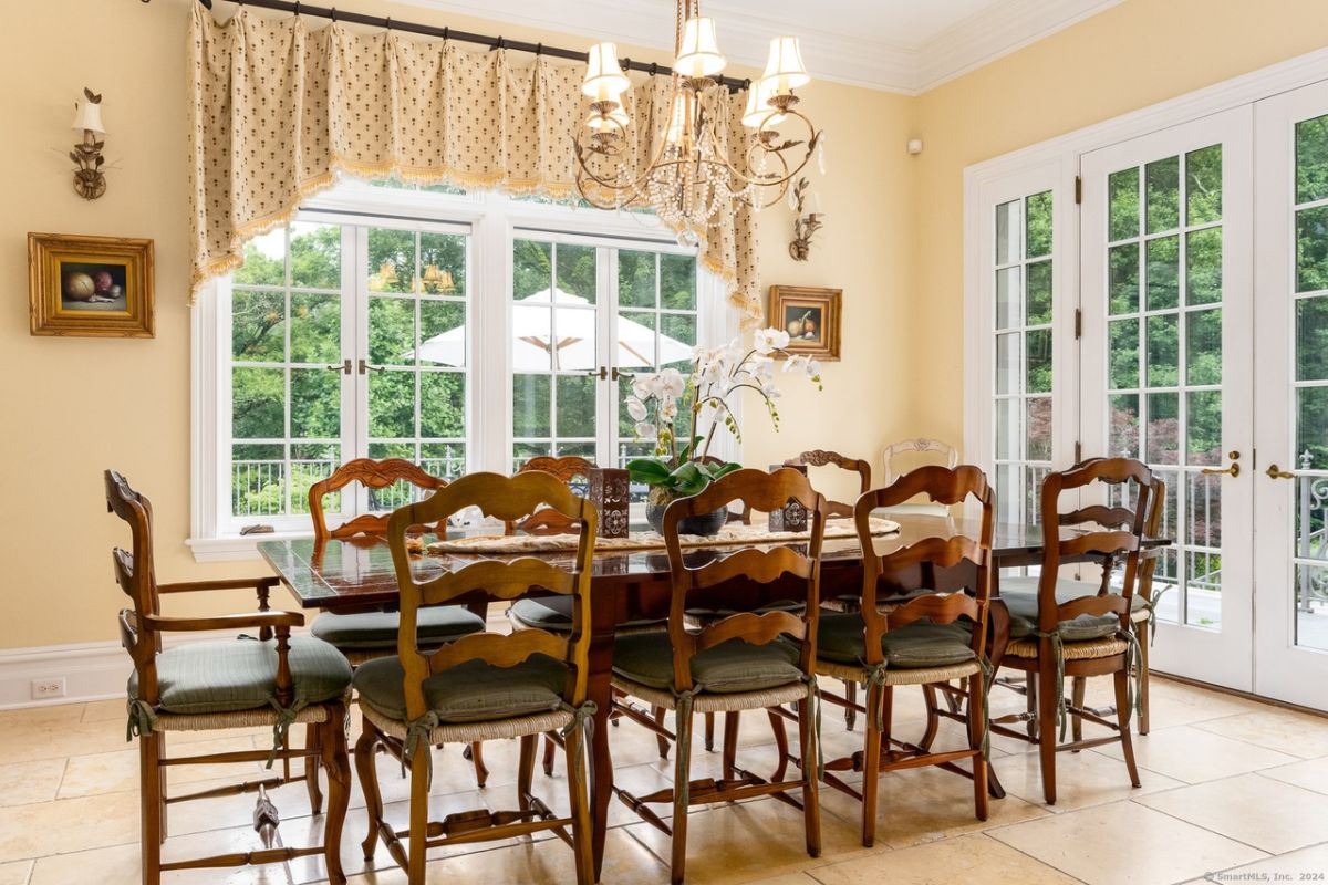 A dining room with windows, a chandelier, and a dining table surrounded by chairs.