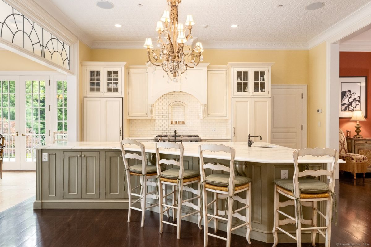 A kitchen with a chandelier, countertops, chairs, sink, and cabinets.