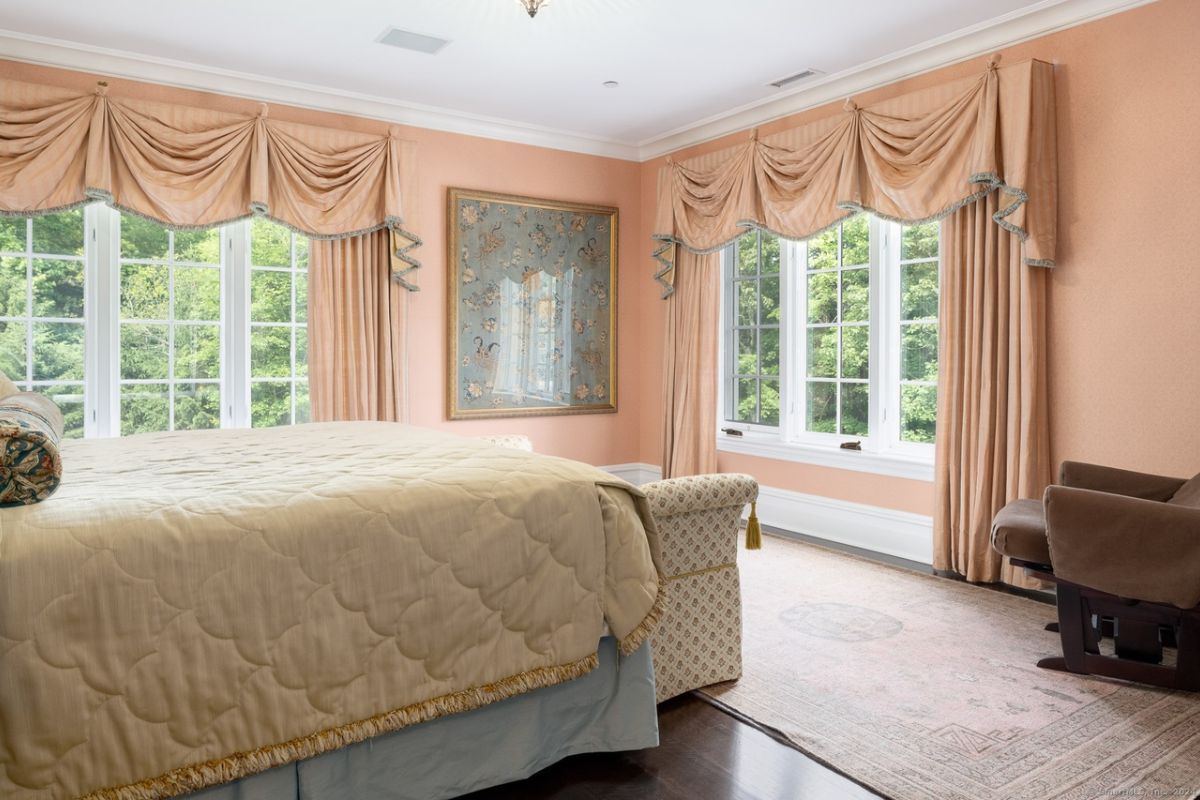 A bedroom with a bed, pink walls, a painting, a window, and a chair.